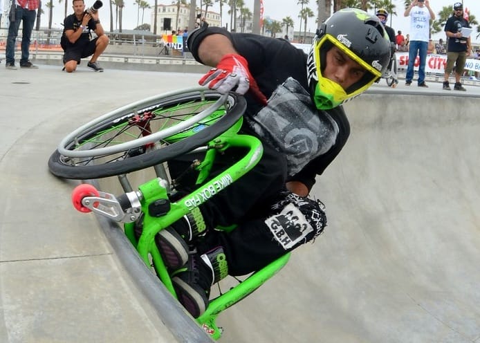 A wheelchair user riding a pool at a skate park wearing a helmet.